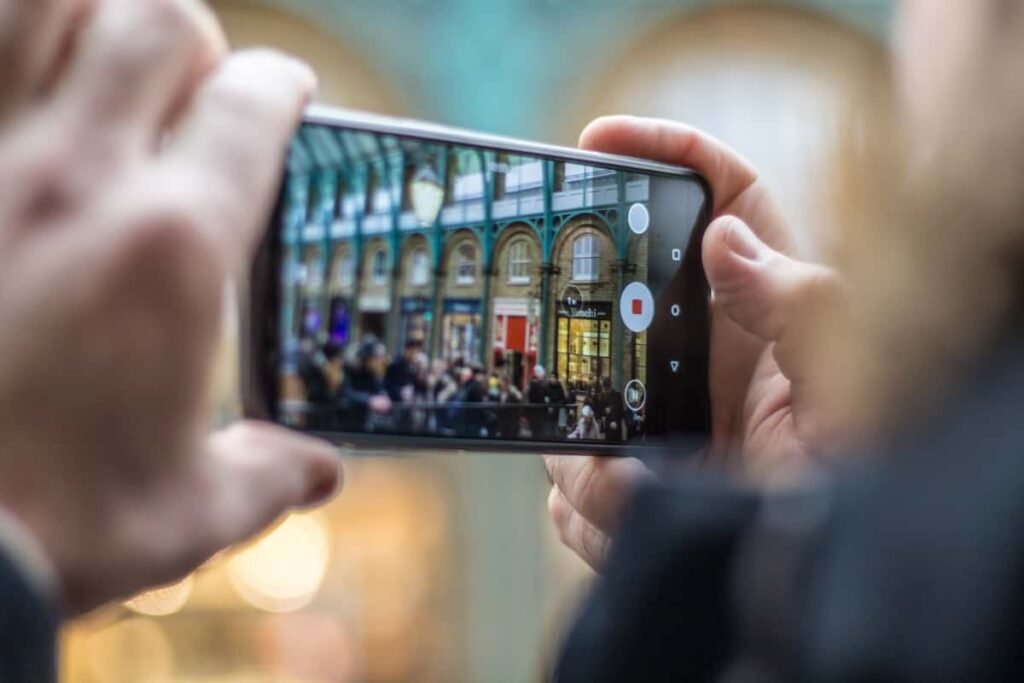 photo of two hands holding a cell phone screen that is taking a photo of a crowd