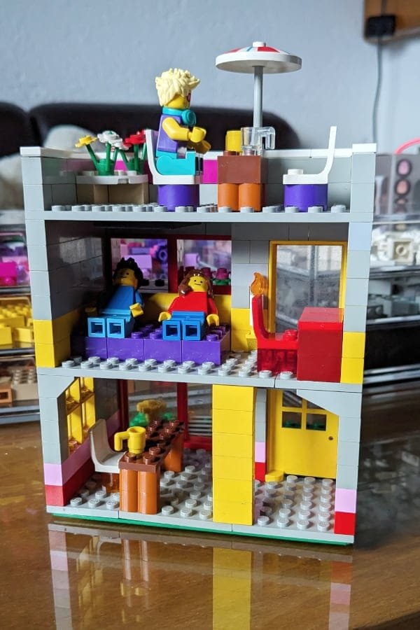 a photo of a furnished LEGO house with a ground floor kitchen, a bedroom on the first floor and a table on the rooftop