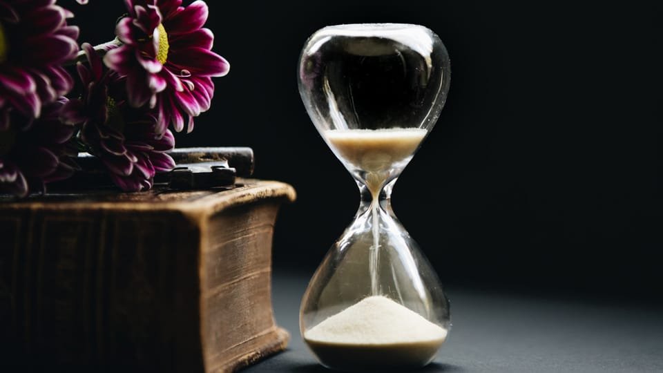 a photo of an hourglass with sand falling down set against a dark backdrop